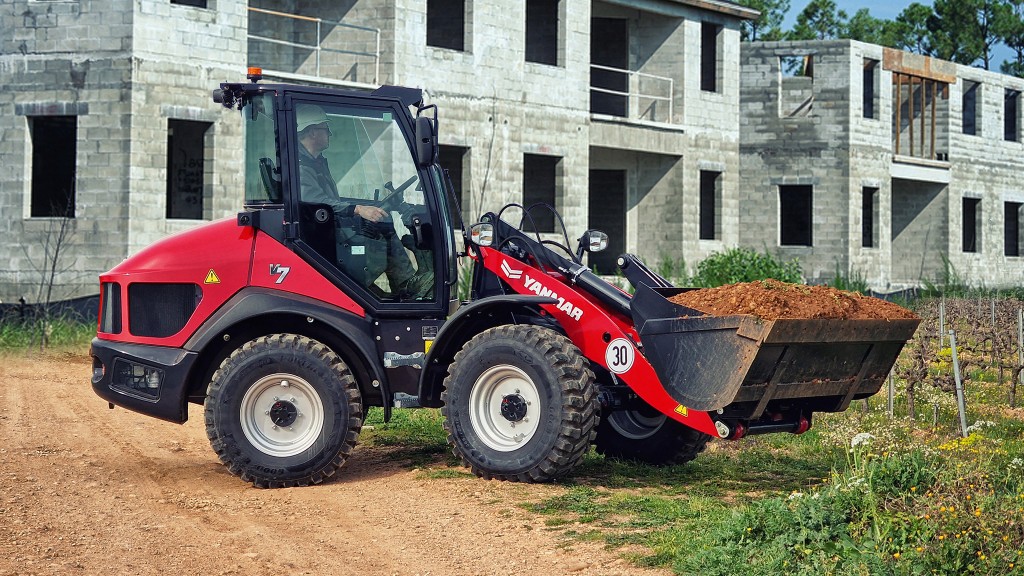 A red compact loader carrying material across a lawn.