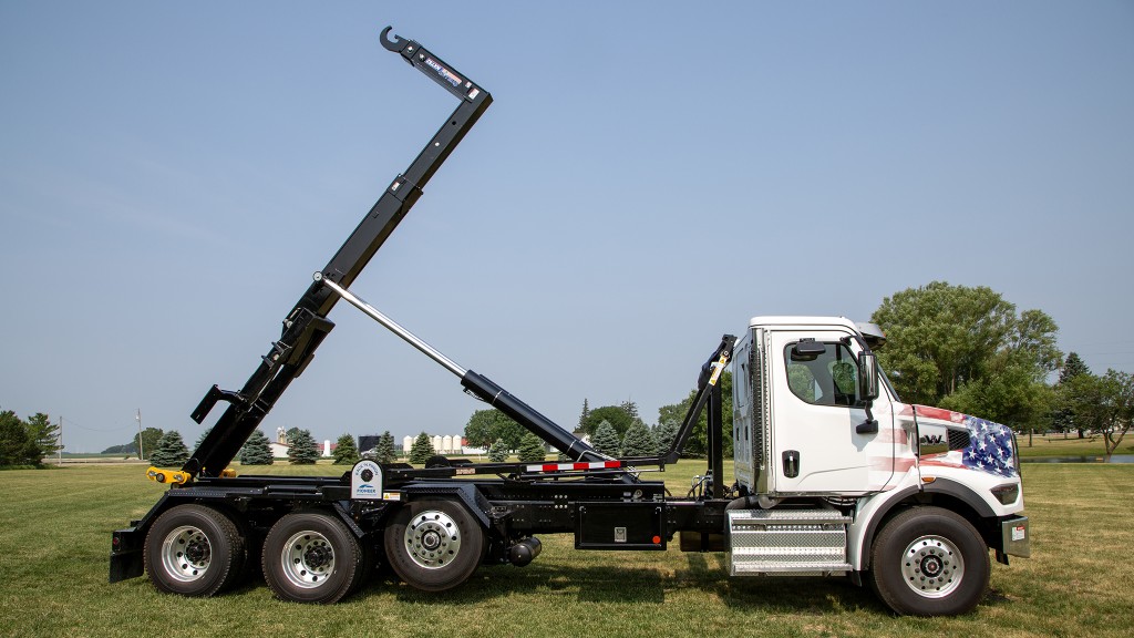 A hooklift truck with lift raised on a grassy field.