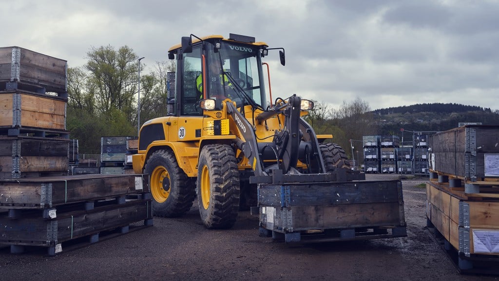 A compact wheel loader carrying a box through stacks of pallets and other material.