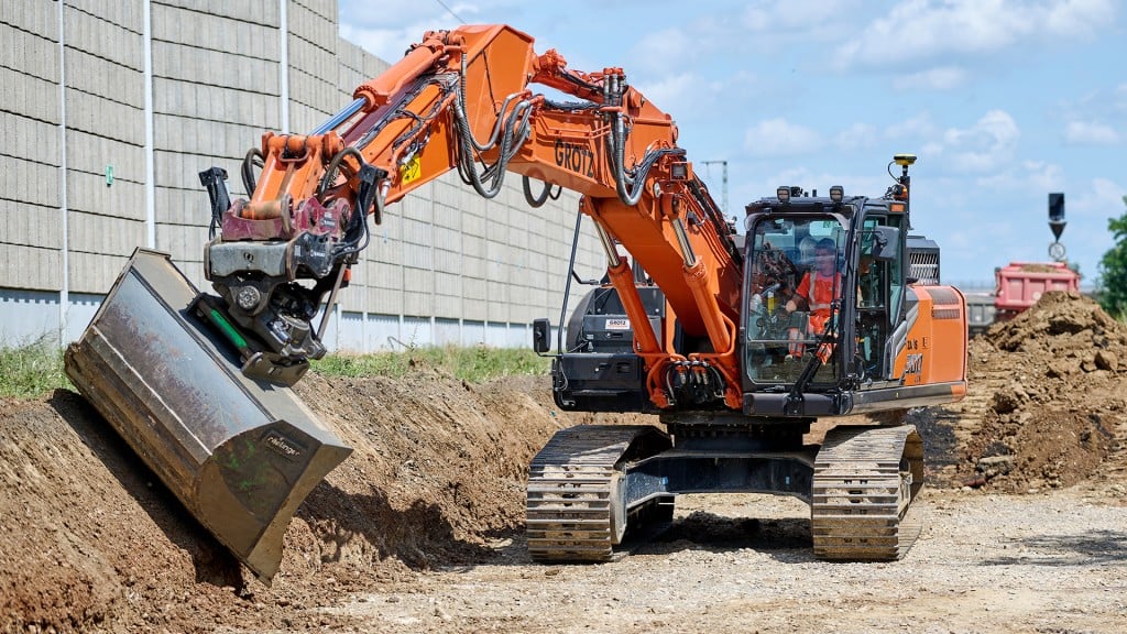 A large excavator works sloping a bank on a job site.