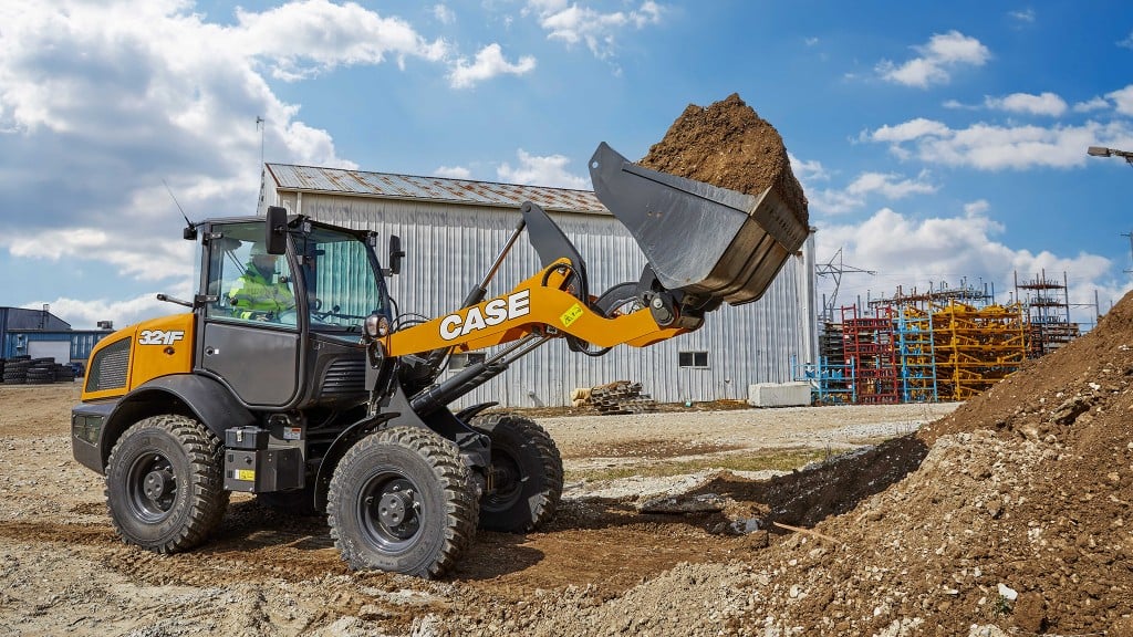 A compact wheel loader scoops dirt from a pile.