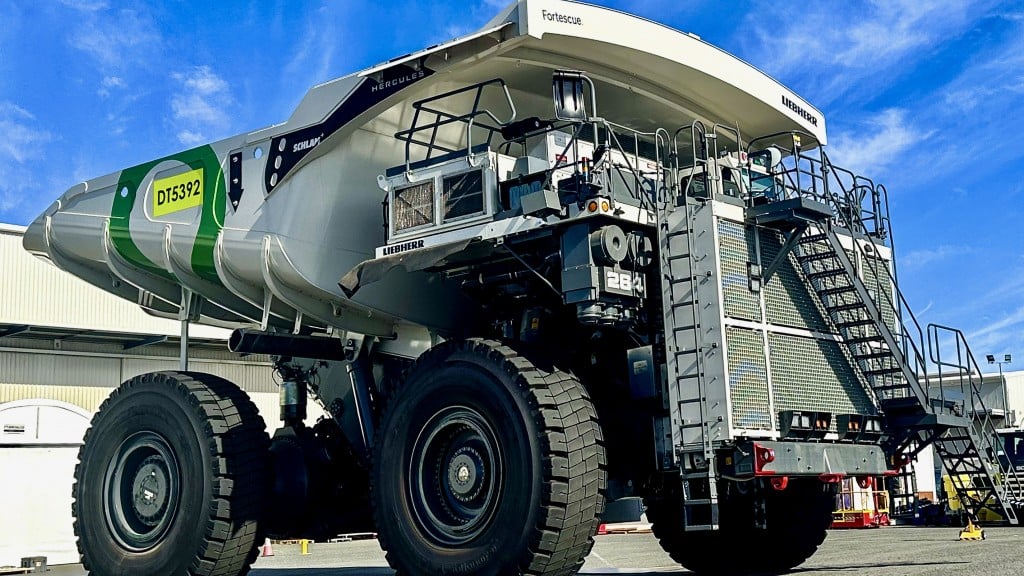 A large white mining truck with green highlights parked outside a shop.