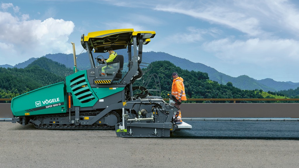 An asphalt paver viewed from the side placing a mat of asphalt along a road surface.