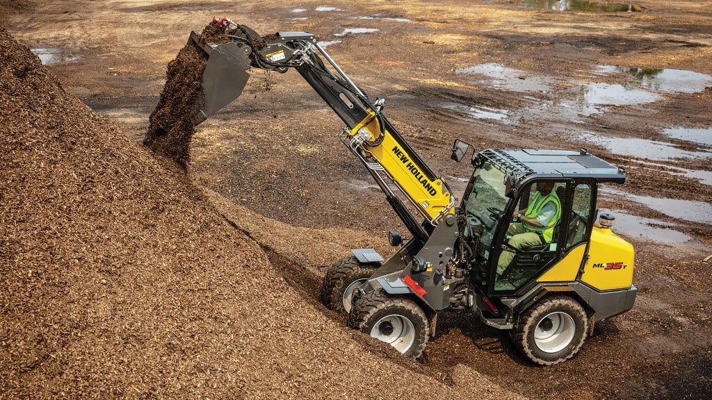 A small articulated loader with a telescopic boom dumps dirt on a pile.