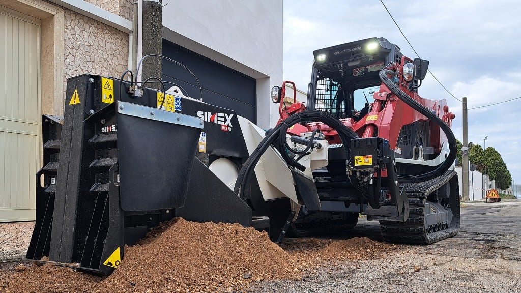A compact track loader uses a wheel saw attachment on a roadway.