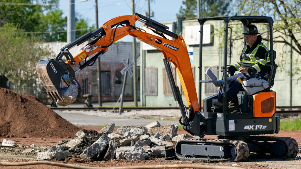 A mini excavator lifts up a rock on a job site