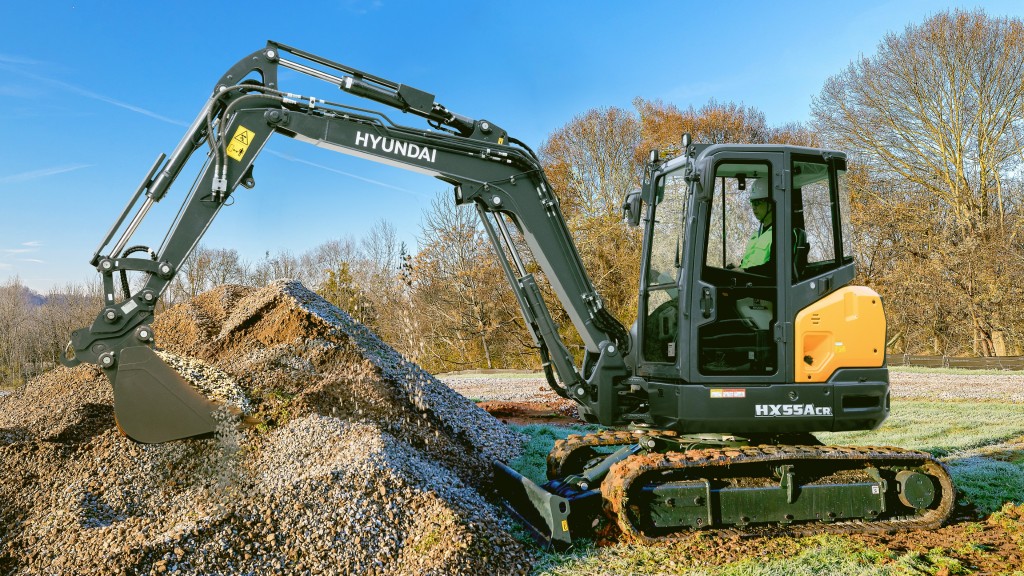 A compact excavator moves a bucket of rocks on a job site