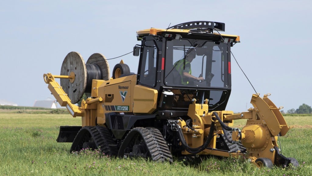 A tracked ride-on tractor working in a field with a cable spool mounted.