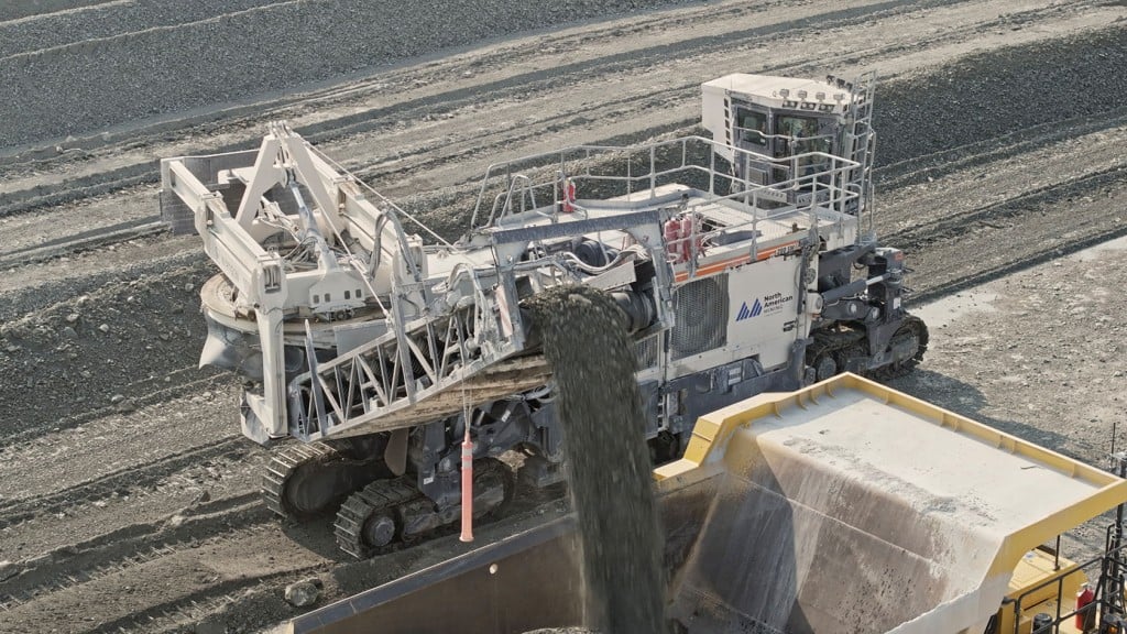 A surface mining machine fills a dump truck while cutting rock.