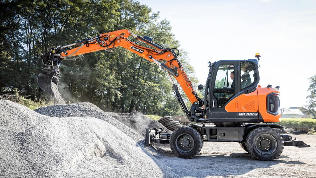 A wheeled mini excavator dumps out a bucket of gravel