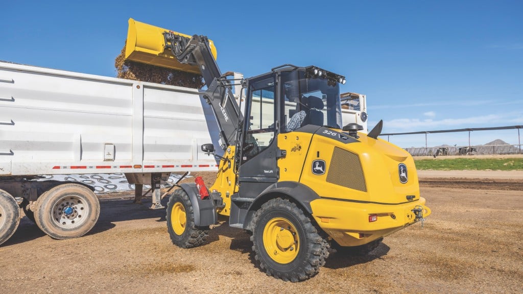 A compact telescopic wheel loader dumps material into a truck