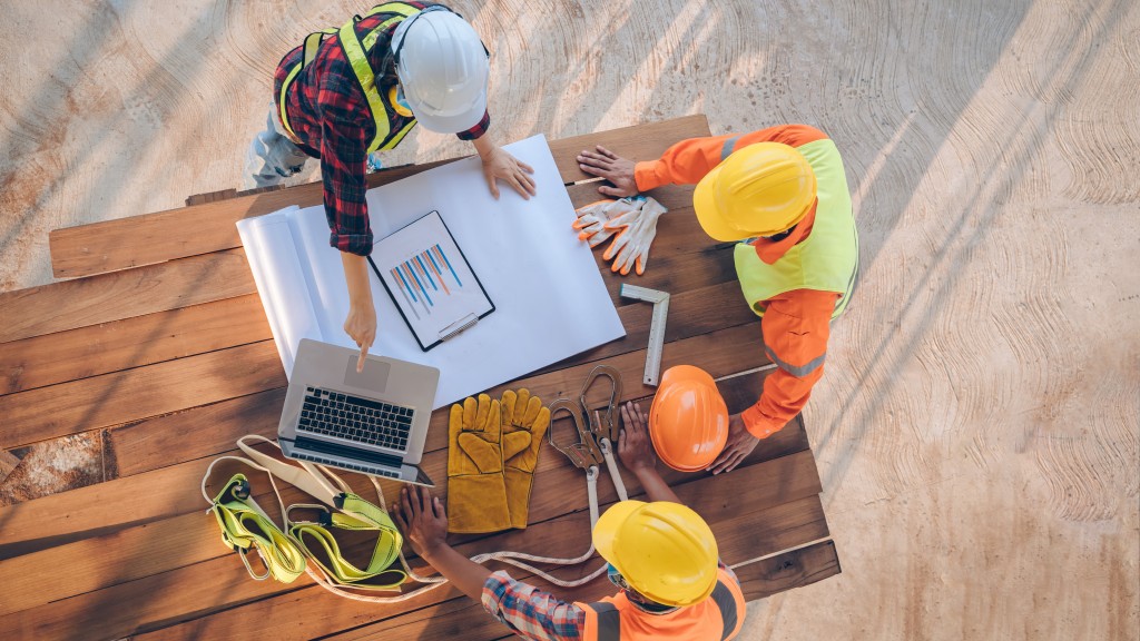 A group of three construction workers look at a laptop on a job site