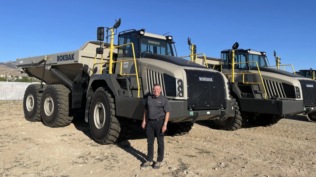 Greg Gerbus stands near two articulated dump trucks