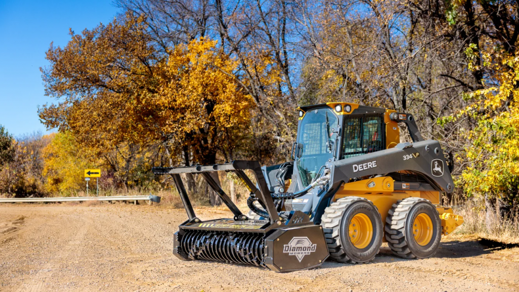 A yellow compact track loader driving onto a field with fall foliage