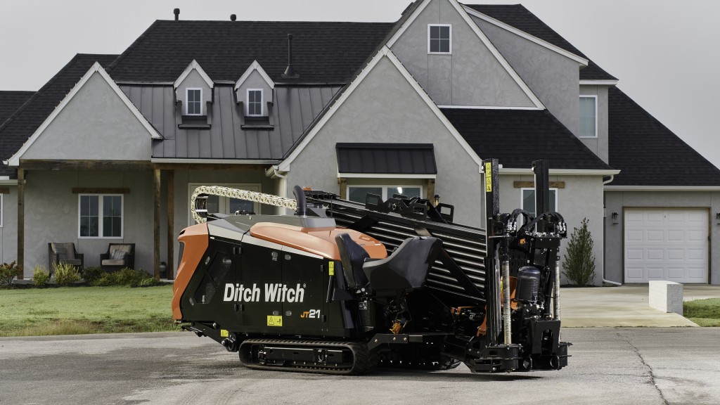 A black and yellow horizontal directional drill on the street in front of a large house