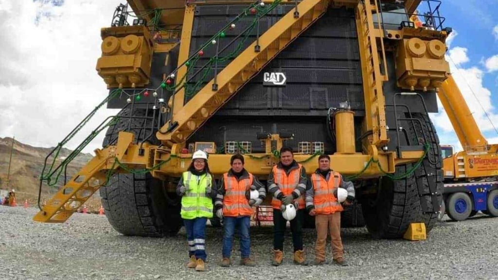 Four Peruvian miners standing in front of a large Caterpillar mining truck