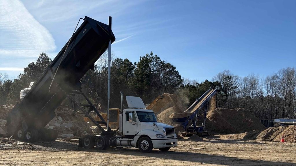 A large dump truck unloads a pile of wood waste