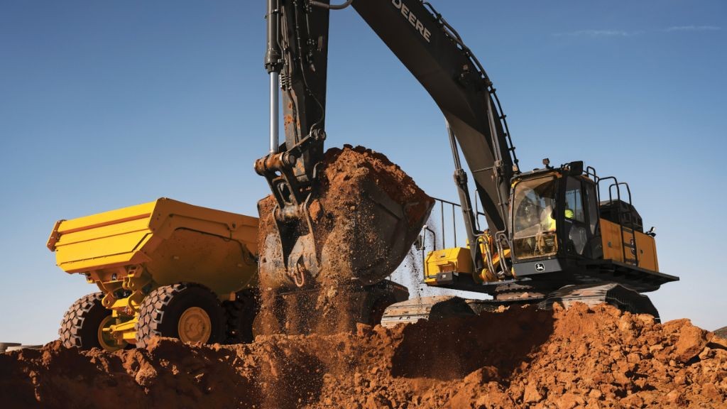 A large excavator digging into a pile of dirt next to a hauling vehicle A large excavator digging into a pile of dirt next to a hauling vehicle