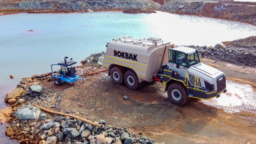A large articulated hauling truck next to a small body of water A large articulated hauling truck next to a small body of water