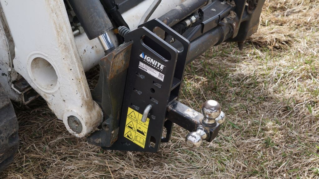 A small trailer loader attached to a compact machine sitting on dry grass