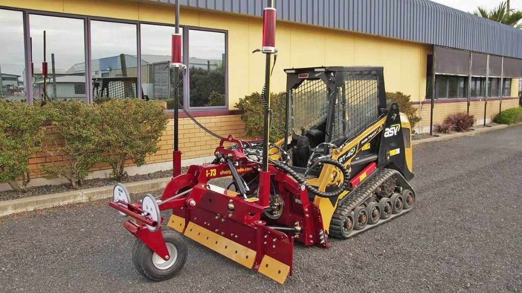 A yellow compact track loader outfitted with a red grader blade