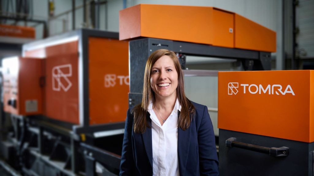 A woman wearing a blue blazer and posing for a head shot in front of a large recycling sorting machine