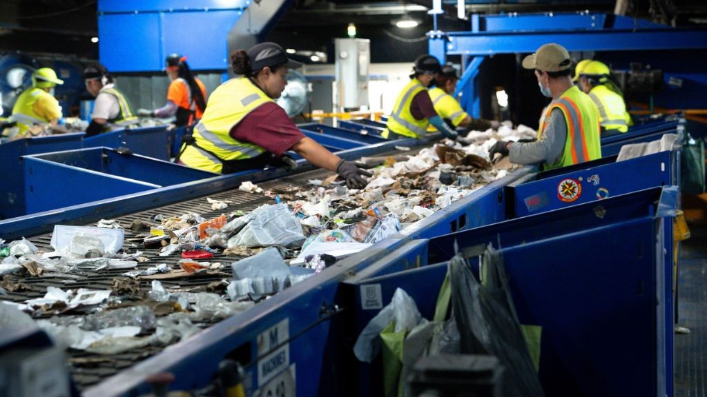 Several people sorting through recycling on an assembly line Several people sorting through recycling on an assembly line