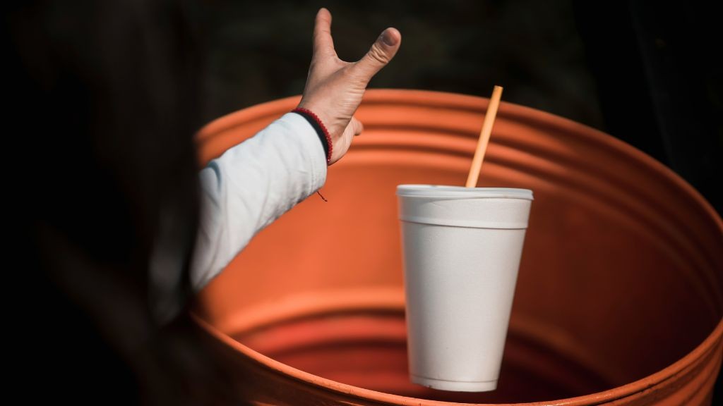 A woman placing a styrofoam cup in a receptacle A woman placing a styrofoam cup in a receptacle