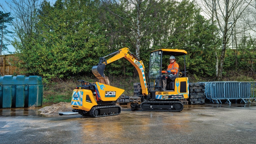 An electric mini excavator fill an electric mini dumper in front of some trees on a small industrial yard An electric mini excavator fill an electric mini dumper in front of some trees on a small industrial yard