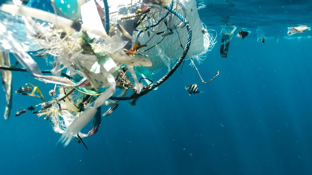 Plastic garbage floating in the ocean with tropical fish swimming near