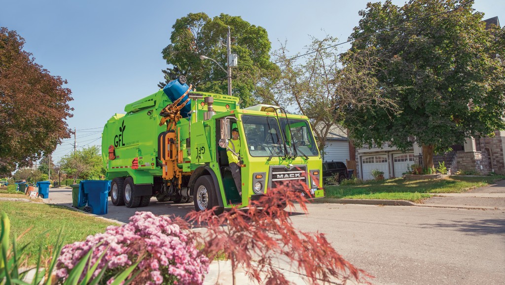 A large green GFL services vehicle behind a bush with pink flowers A large green GFL services vehicle behind a bush with pink flowers