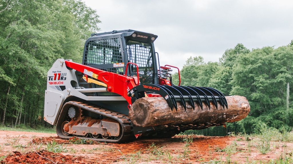 A red compact track loader holding a large log using a grapple attachment