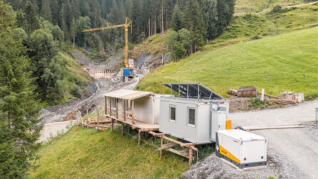 A view of a crane in the valley of two mountains with a generator on the crest of the hill