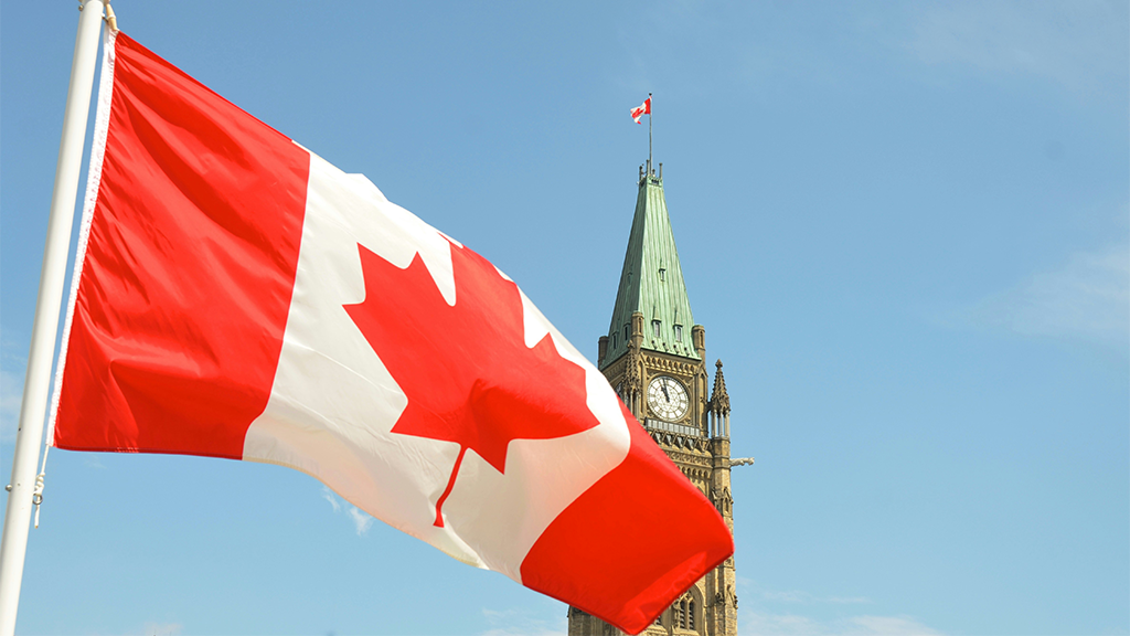 The Canadian flag waving in front of the Parliament building