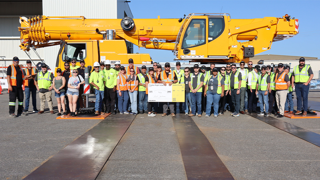 A group of people taking a photo with a large cheque in front of a mobile crane