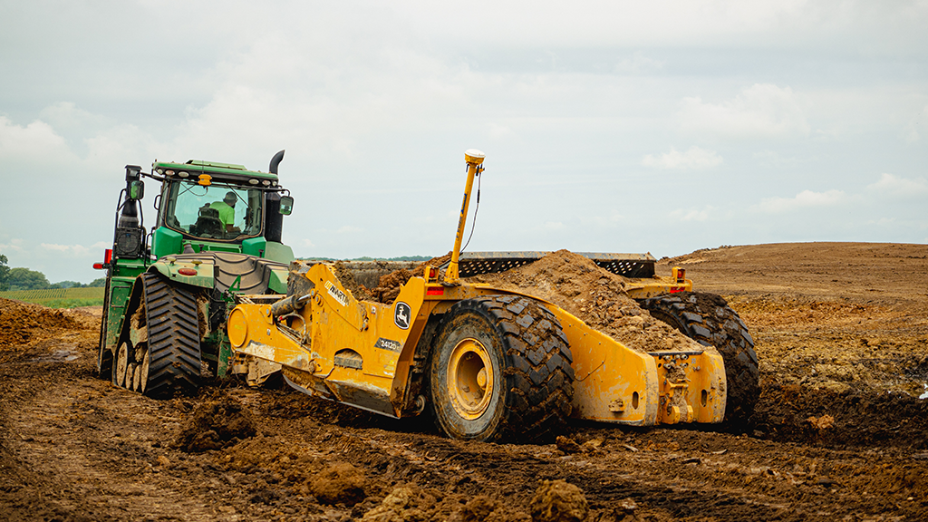 A tractor towing a scraper on an outdoor site A tractor towing a scraper on an outdoor site