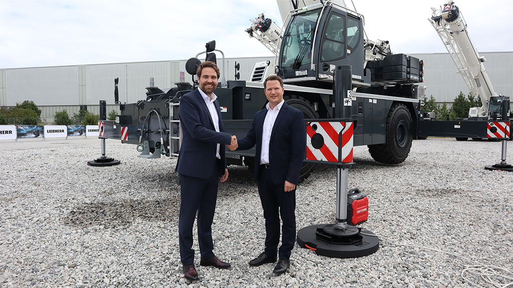 Two men shaking hands in front of a mobile crane