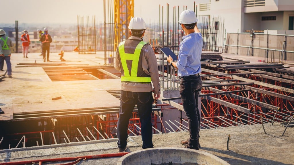 Two men stand on a construction site while reading a tablet Two men stand on a construction site while reading a tablet