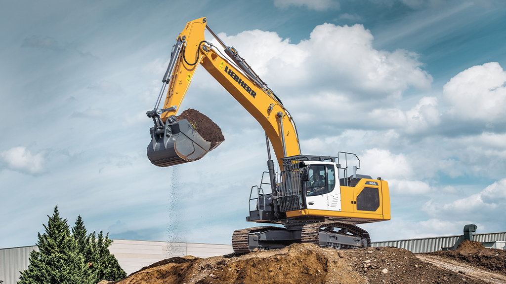 An excavator lifts a bucket filled with aggregates on an outdoor site