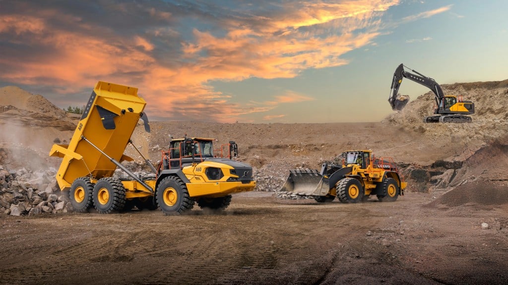 An articulated dump truck unloads aggregates onto a construction site next to a wheel loader and an excavator