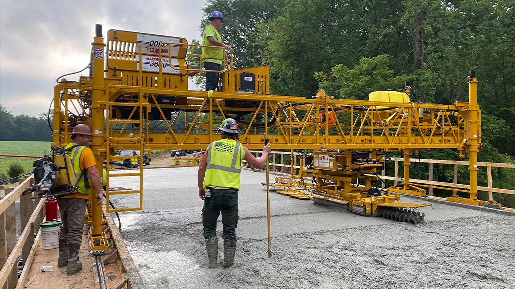 Several men work on freshly poured concrete with a floating bridge