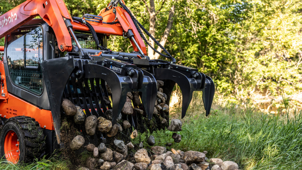 A compact track loader outfitted with a grapple moves rocks