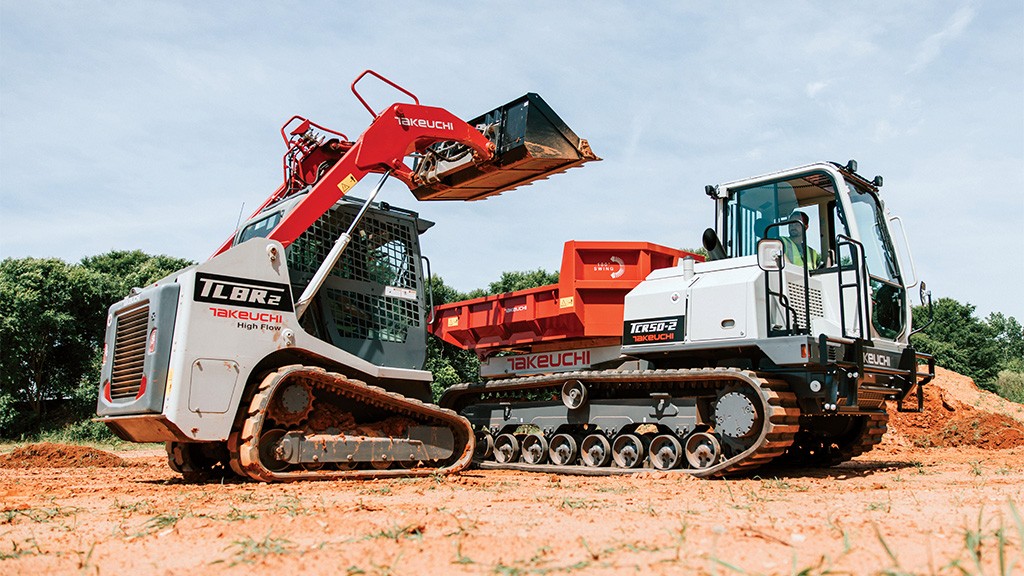 A compact track loader fills a hauler with aggregates from a bucket attachment