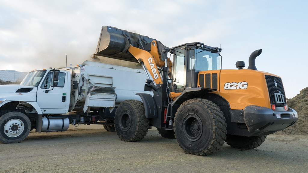 A wheel loader a bucket filled with materials into the back of a dump truck A wheel loader a bucket filled with materials into the back of a dump truck