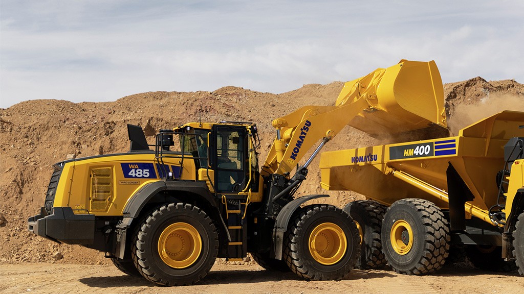 A wheel loader dumps a bucket of material into the back of a hauler