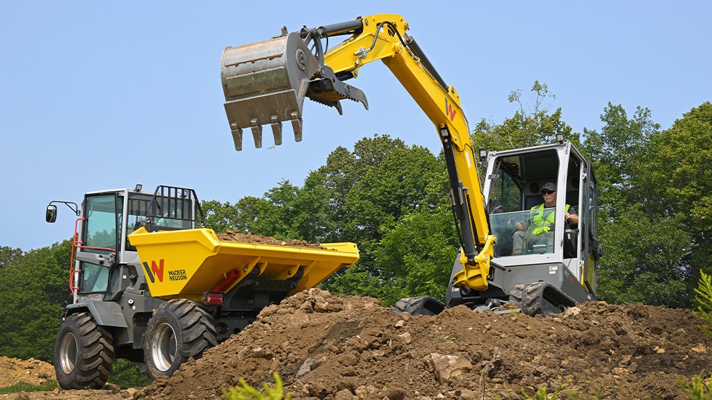 A compact tracked excavator fills the bed of a site dumper