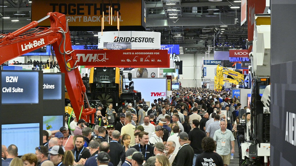 The inside of a large trade show with many people walking underneath hanging banners for brands and equipment