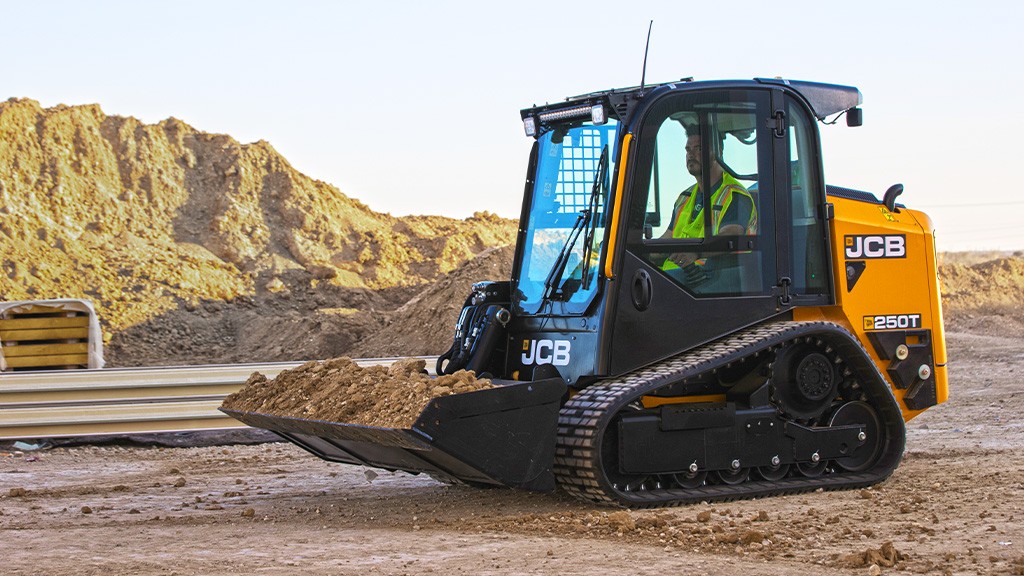 A man operates a compact track loader with a bucket attachment