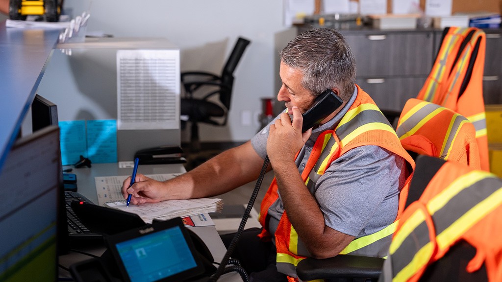 A man sits at a desk and speaks into a phone