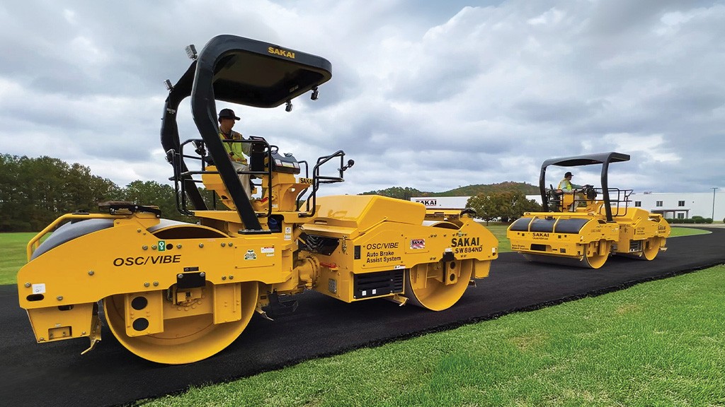 Two yellow tandem rollers work on a freshly paved road